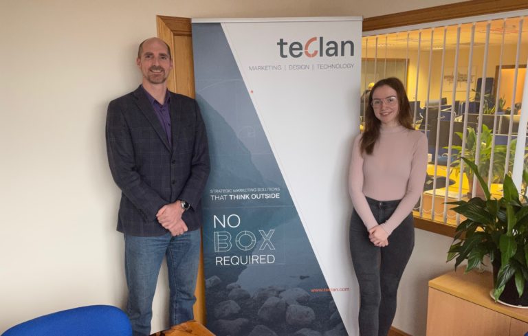Fergus Weir and Caitlin Maclean stand in front of teclan sign
